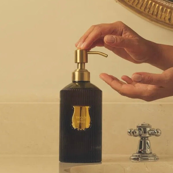 Hand using a black soap dispenser with gold accents in a bathroom setting.